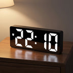 Slim black mirror-front alarm clock on a walnut nightstand at night, its white LED digits reading 22:10