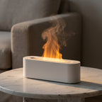 White pill-shaped flame-effect diffuser switched on atop a marble side table, an amber-lit plume of mist rising from its slot
